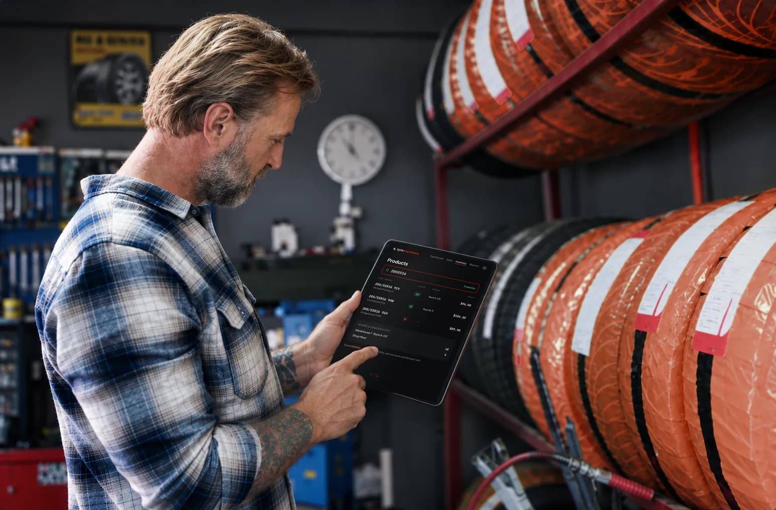 A mechanic checks tyre stock on a tablet in front of a tyre rack